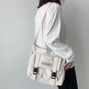 Detailed side view of off-white canvas messenger bag with black plastic buckle closures