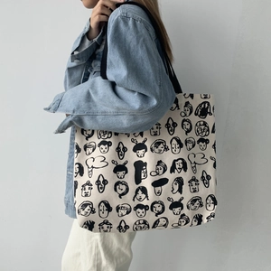 Detail of large canvas tote bag featuring whimsical cartoon faces and black wide straps