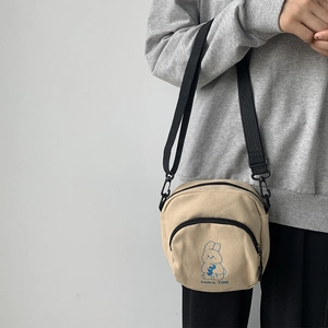 Detail of cute beige canvas crossbody bag featuring a blue cartoon rabbit and snack time text