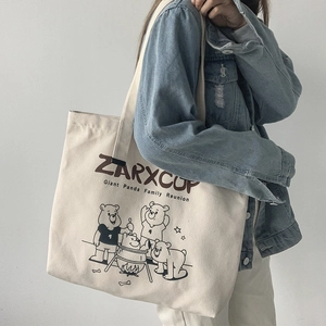 Detail of cream canvas tote bag with cartoon bear illustration on a model's shoulder