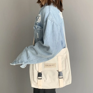 Detail of beige nylon messenger bag showing flap closure with black buckles and leather logo