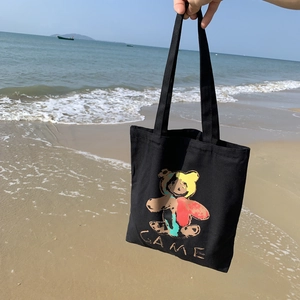 Sac cabas en toile noire avec ours coloré sur fond de plage ensoleillée et mer
