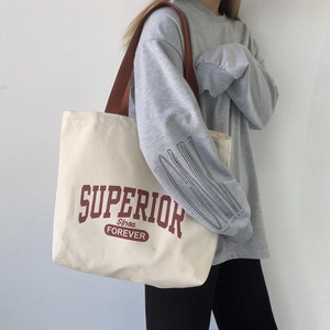 Detail shot of off-white canvas tote bag with red Superior lettering and brown handles