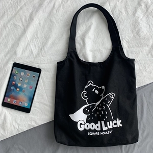 Detail of black canvas tote bag with white cartoon bear and Good Luck lettering