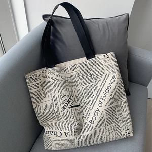 Close-up of retro newspaper print canvas tote bag on a grey fabric sofa setting