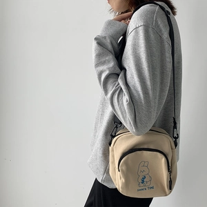 Detail of beige canvas crossbody bag featuring a cartoon rabbit and Snack Time text