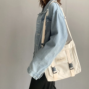 Detail of cream canvas messenger bag with dual buckles and logo patch worn by model