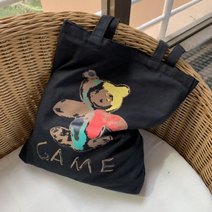 Détail du sac cabas en toile noire avec imprimé ours artistique et texte GAME sur chaise rotin