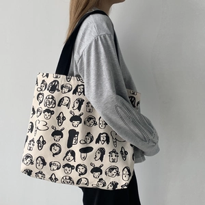 Side view of a large cream canvas tote bag with black line art cartoon portraits