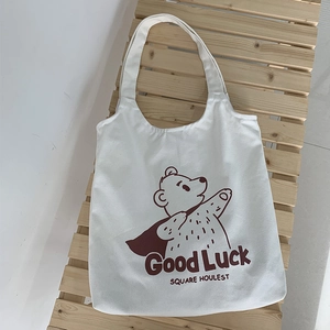 Close-up of white canvas tote bag with a brown cartoon bear print on a wooden bench