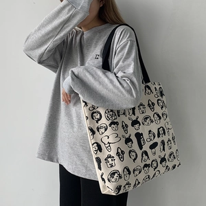 Detailed view of the large canvas tote bag with black cartoon face prints worn on shoulder