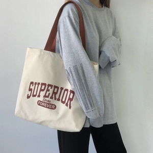Detailed shot of large canvas tote bag with red varsity lettering and brown handles