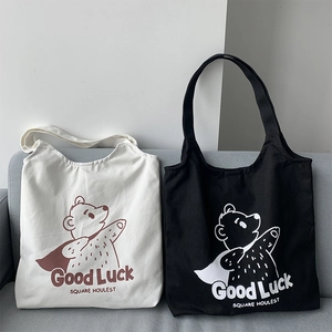 Detail of canvas tote bags in cream and black with cartoon bear and Good Luck print