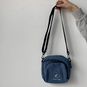 Detail of blue canvas messenger bag with cute cartoon rabbit and snack time print