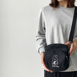 Close-up of black canvas crossbody bag featuring a cute cartoon rabbit and snack time text