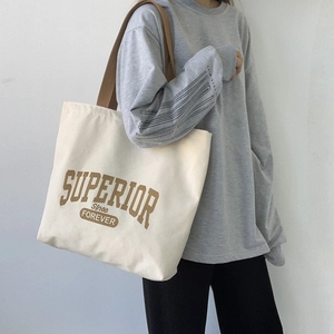 Detail of a large cream canvas tote bag with brown lettering and wide shoulder straps
