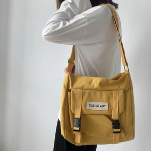 Detail of yellow canvas crossbody bag featuring a front buckle strap and adjustable webbing