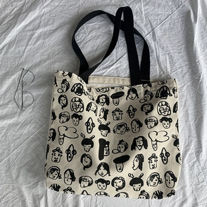 Close-up of cream canvas tote bag featuring black cartoon face patterns and cotton handles