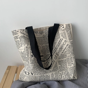 Close-up of a large canvas tote bag with retro English newspaper print and black straps