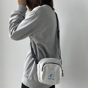 Detail of white canvas crossbody bag featuring a cute cartoon rabbit and snack time print