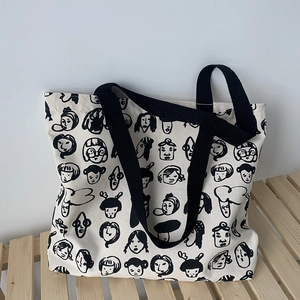 Detail of large canvas tote bag featuring artistic black cartoon face prints on off-white fabric