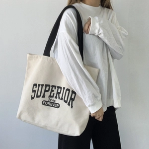 Close-up of white canvas tote bag with black strap and vintage letter print on shoulder
