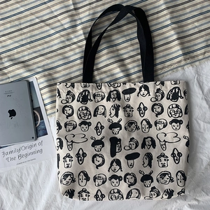 Detail of off-white canvas tote bag featuring black artistic face graffiti and woven straps