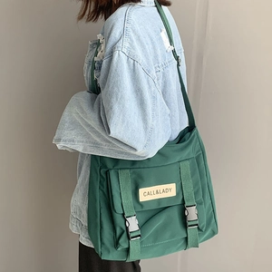 Detail of dark green canvas messenger bag featuring plastic buckles and logo patch