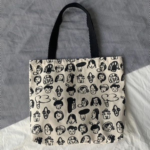 Close-up of beige canvas tote bag featuring minimalist black cartoon face print