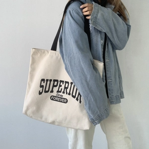Close-up of cream canvas tote bag with black vintage lettering and black shoulder straps