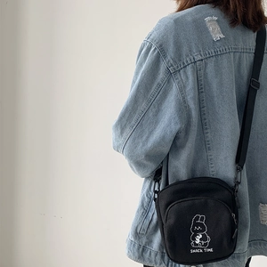 Close-up of a small black canvas crossbody bag with a white rabbit print on a model