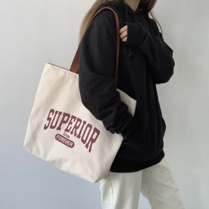 Close-up of off-white canvas tote bag with red Superior Forever lettering on a model