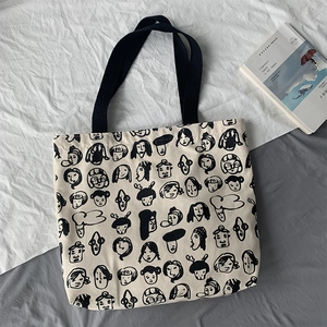 Detail of beige canvas tote bag with black graffiti face patterns and fabric handles