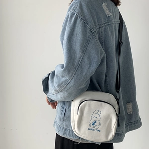 Detail of white canvas crossbody bag featuring blue cartoon rabbit and snack time print
