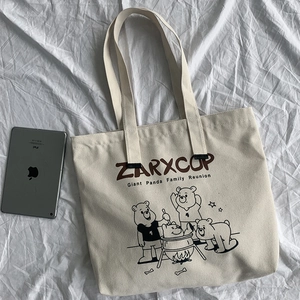 Detail of beige canvas tote bag with panda campfire illustration and iPad for size comparison