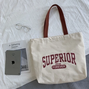 Retro canvas tote bag with brown handles, red typography, and casual lifestyle props