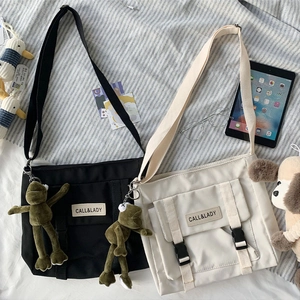 Detailed view of canvas messenger bags in black and beige with cute plush frog charms