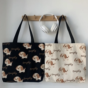 Dettaglio di borse tote in tela nera e beige con stampe di cuccioli e manici in tessuto