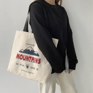 Lifestyle view of a minimalist cream canvas tote bag with mountain print and black straps