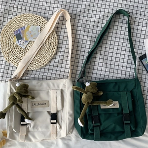 Detail of canvas messenger bags in beige and green with buckle and plush charm