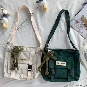 Close-up of beige and green canvas messenger bags with frog charms and flip buckles