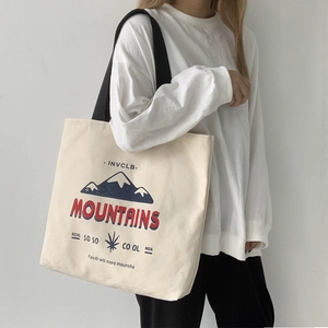 Detail of off-white canvas tote bag featuring mountain print and black shoulder straps