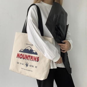 Detail view of cream canvas tote bag with mountain graphic and black shoulder strap