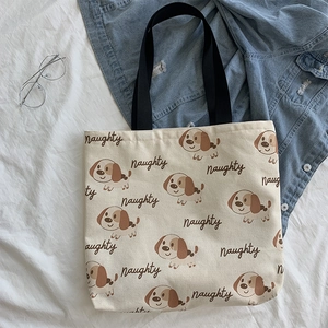 Dettaglio borsa in tela beige con stampa di cagnolini e tracolle nere su tessuto