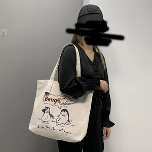 Canvas tote bag with cute penguin print and artistic red text shown in use