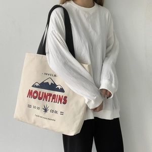 Detail of off-white canvas tote bag featuring vintage mountain print and black wide strap