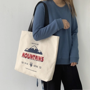 Detail view of canvas tote bag showing mountain print and black shoulder strap on model