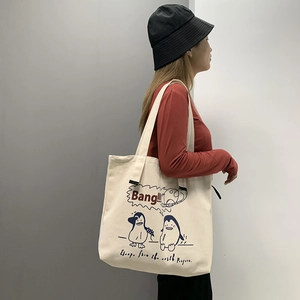 Detail of cream canvas tote bag featuring cartoon penguin print and large capacity design