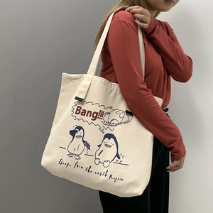 Detail view of large off-white canvas tote bag with blue penguin cartoon and wide strap