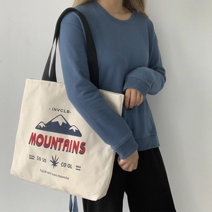 Detail of a white canvas tote bag featuring a blue mountain graphic and black shoulder strap